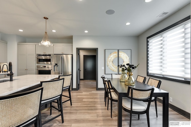 dining space featuring light hardwood / wood-style flooring, sink, and a notable chandelier