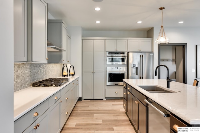 kitchen featuring sink, appliances with stainless steel finishes, light hardwood / wood-style flooring, backsplash, and decorative light fixtures