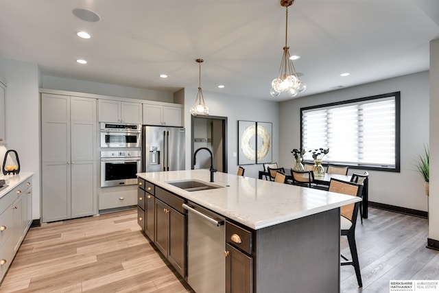 kitchen featuring decorative light fixtures, appliances with stainless steel finishes, light hardwood / wood-style floors, a center island with sink, and sink