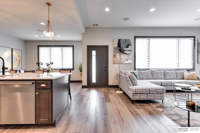 kitchen with stainless steel dishwasher, an inviting chandelier, hanging light fixtures, light wood-type flooring, and sink