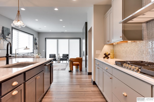 kitchen featuring decorative light fixtures, tasteful backsplash, light hardwood / wood-style flooring, wall chimney range hood, and sink