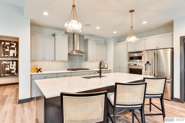 kitchen featuring an island with sink, stainless steel appliances, wall chimney exhaust hood, and light hardwood / wood-style floors