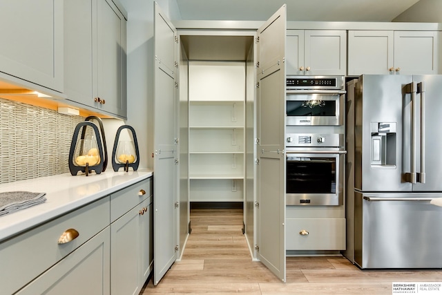 kitchen featuring backsplash, gray cabinets, appliances with stainless steel finishes, and light wood-type flooring