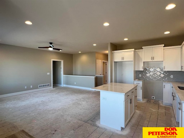 kitchen with white cabinetry, ceiling fan, light tile flooring, a center island, and tasteful backsplash