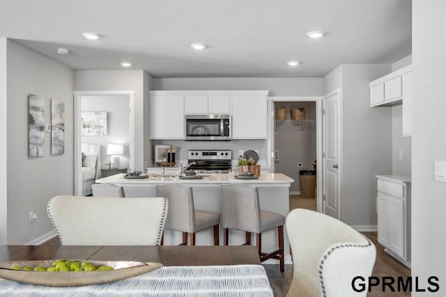 kitchen featuring range, an island with sink, white cabinetry, hardwood / wood-style floors, and a breakfast bar