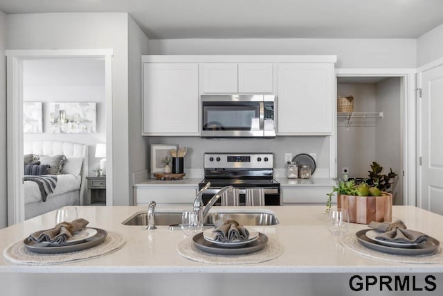 kitchen with sink, appliances with stainless steel finishes, white cabinetry, and light stone counters