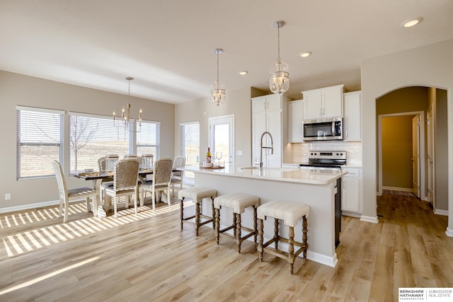 kitchen featuring sink, stainless steel appliances, an island with sink, decorative light fixtures, and white cabinets