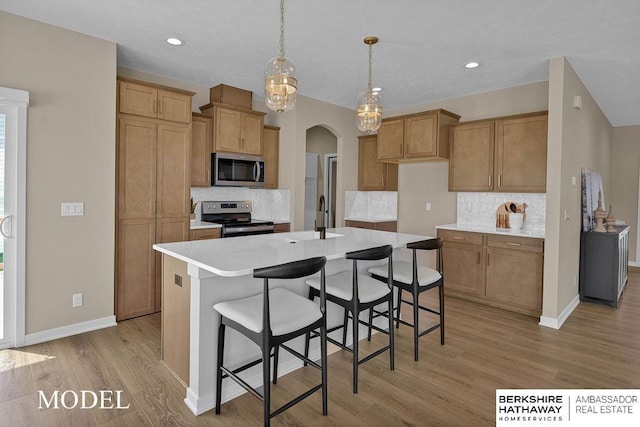 kitchen with light hardwood / wood-style flooring, an island with sink, tasteful backsplash, decorative light fixtures, and stainless steel appliances