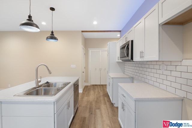 kitchen with a center island with sink, appliances with stainless steel finishes, hanging light fixtures, light wood-type flooring, and sink