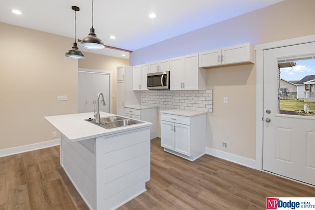 kitchen with decorative light fixtures, wood-type flooring, sink, an island with sink, and white cabinets