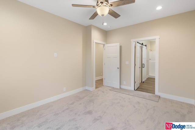 unfurnished bedroom with a barn door, light colored carpet, and ceiling fan