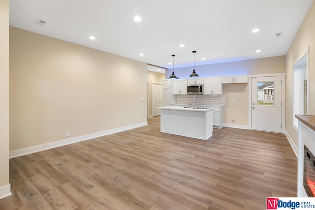 kitchen with hanging light fixtures, backsplash, a center island with sink, white cabinetry, and light wood-type flooring