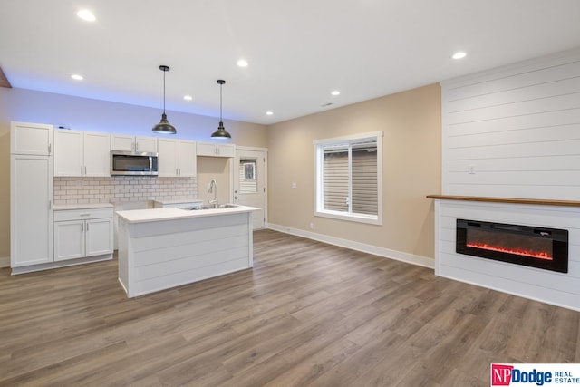 kitchen featuring white cabinets, hanging light fixtures, sink, and light hardwood / wood-style flooring