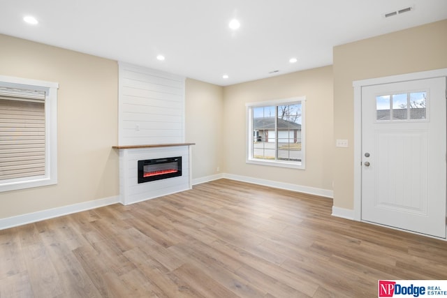 unfurnished living room with a fireplace, light wood-type flooring, and plenty of natural light