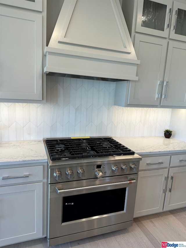 kitchen with light stone countertops, decorative backsplash, stainless steel stove, custom exhaust hood, and light wood-type flooring