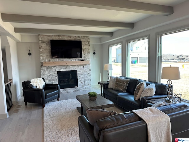 living room featuring beam ceiling, a stone fireplace, and light wood-type flooring