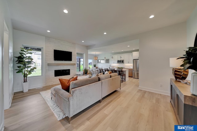 living room featuring light hardwood / wood-style floors, sink, and a stone fireplace