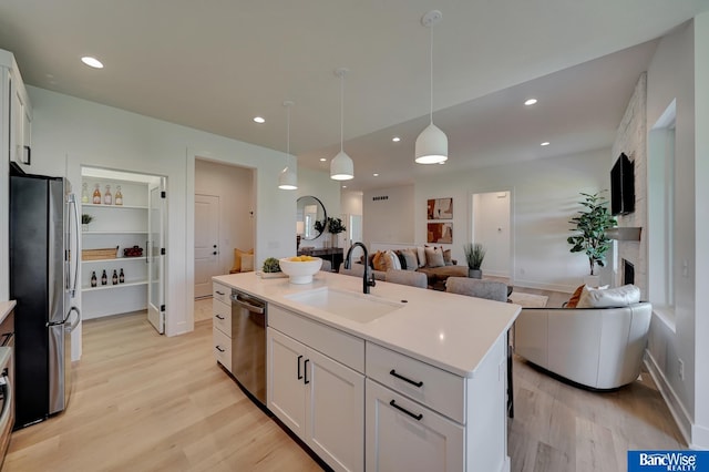 kitchen with stainless steel appliances, white cabinets, sink, light hardwood / wood-style flooring, and a kitchen island with sink