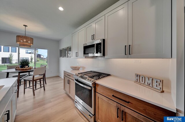 kitchen featuring white cabinetry, pendant lighting, light wood-type flooring, and gas range