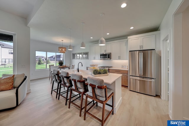 kitchen with a kitchen bar, white cabinets, a kitchen island with sink, light wood-type flooring, and refrigerator