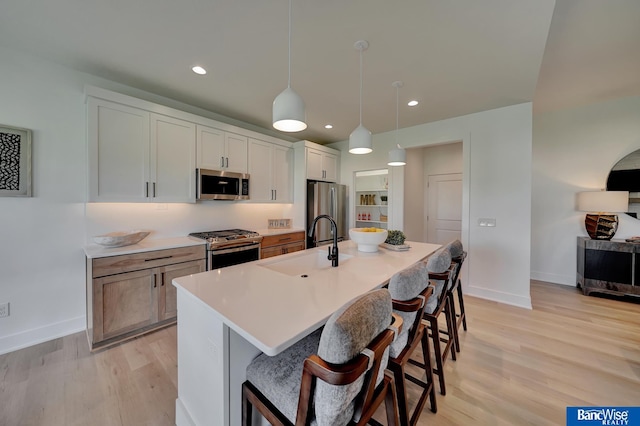 kitchen with appliances with stainless steel finishes, light hardwood / wood-style flooring, hanging light fixtures, and a kitchen island with sink