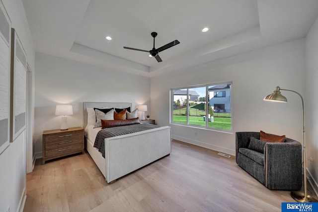 bedroom featuring light hardwood / wood-style flooring, ceiling fan, and a tray ceiling