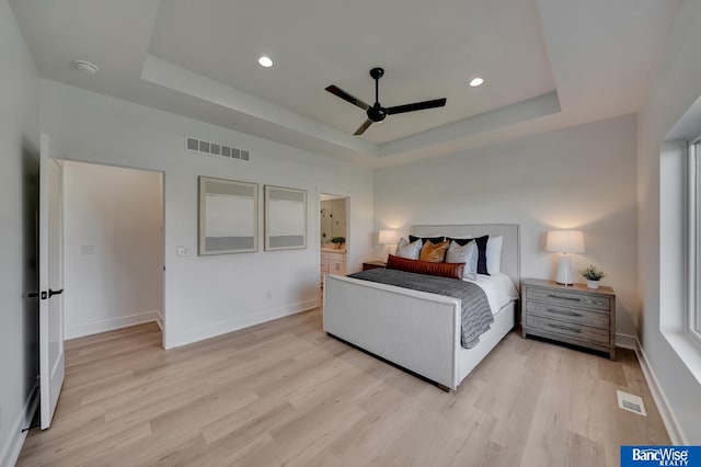 bedroom with light hardwood / wood-style flooring, ceiling fan, and a tray ceiling