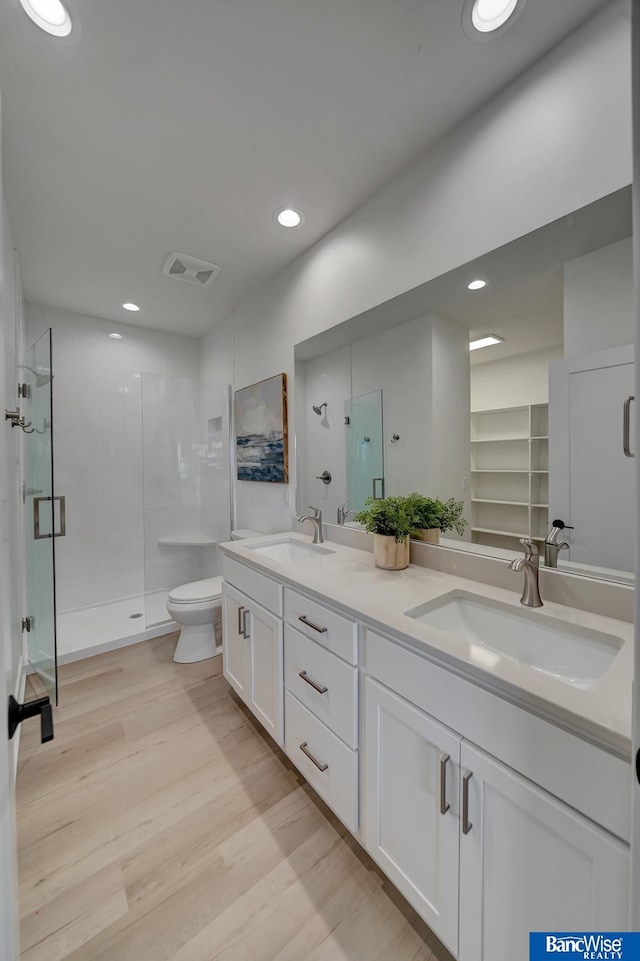 bathroom featuring a shower with shower door, toilet, double sink vanity, and hardwood / wood-style floors