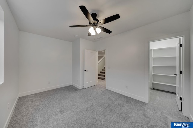 unfurnished bedroom with a closet, light colored carpet, a spacious closet, and ceiling fan