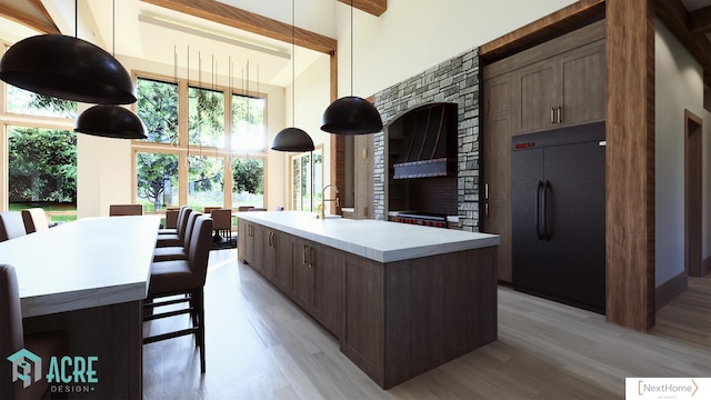 kitchen featuring a center island with sink, dark brown cabinetry, built in fridge, and light hardwood / wood-style flooring