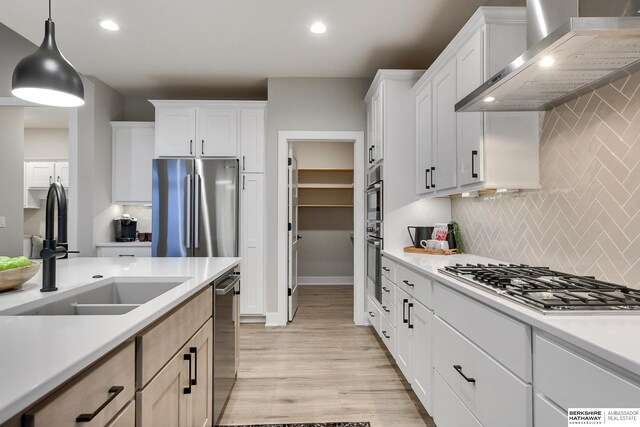 kitchen featuring wall chimney exhaust hood, decorative light fixtures, light wood-type flooring, backsplash, and stainless steel appliances