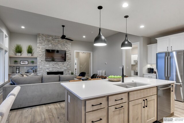 kitchen featuring an island with sink, a stone fireplace, stainless steel appliances, light hardwood / wood-style flooring, and pendant lighting