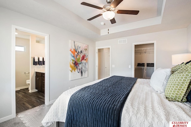 bedroom featuring a closet, ceiling fan, ensuite bathroom, a raised ceiling, and hardwood / wood-style flooring