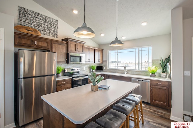 kitchen with decorative light fixtures, dark hardwood / wood-style floors, appliances with stainless steel finishes, vaulted ceiling, and a kitchen island