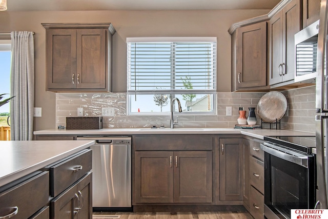 kitchen with appliances with stainless steel finishes, sink, light wood-type flooring, and decorative backsplash