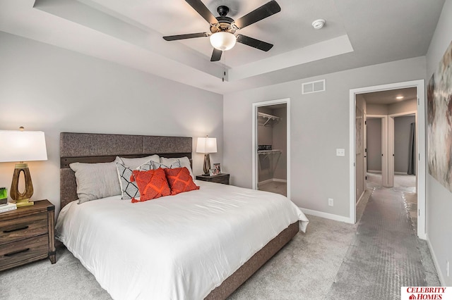 bedroom with light carpet, a closet, a spacious closet, a raised ceiling, and ceiling fan