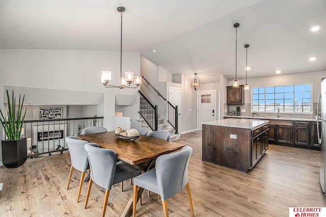 dining area with a chandelier, sink, light hardwood / wood-style floors, and vaulted ceiling