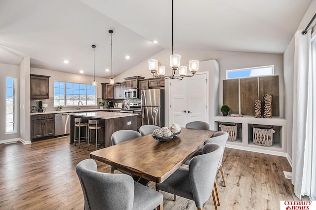 dining area featuring sink, wood-type flooring, a chandelier, and vaulted ceiling