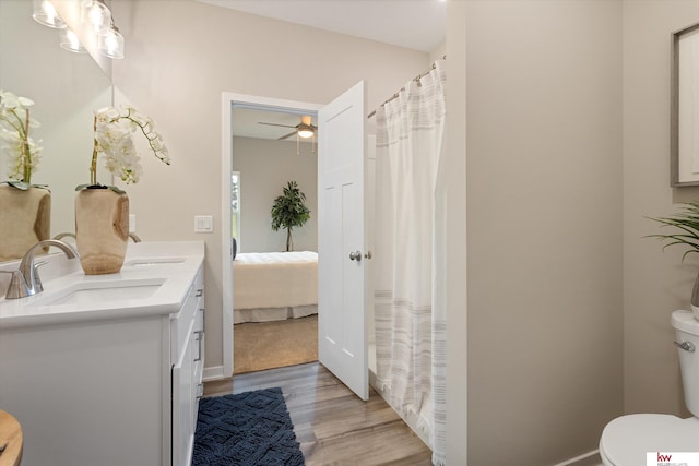 bathroom featuring large vanity, ceiling fan, toilet, hardwood / wood-style flooring, and dual sinks