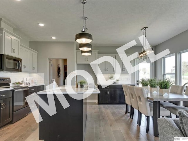 kitchen with pendant lighting, a kitchen island with sink, range with electric stovetop, tasteful backsplash, and light hardwood / wood-style floors