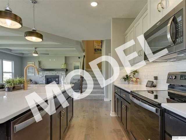 kitchen featuring appliances with stainless steel finishes, a fireplace, backsplash, hanging light fixtures, and light hardwood / wood-style flooring