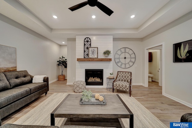 living room with light hardwood / wood-style flooring, ceiling fan, a fireplace, and a tray ceiling