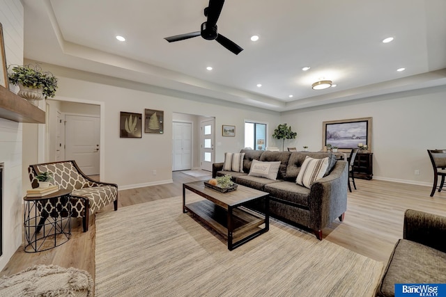 living room featuring a raised ceiling, light hardwood / wood-style floors, and ceiling fan