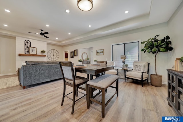 dining space featuring ceiling fan, light wood-type flooring, and a tray ceiling