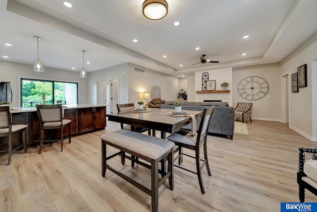 dining space with ceiling fan, a raised ceiling, and light wood-type flooring