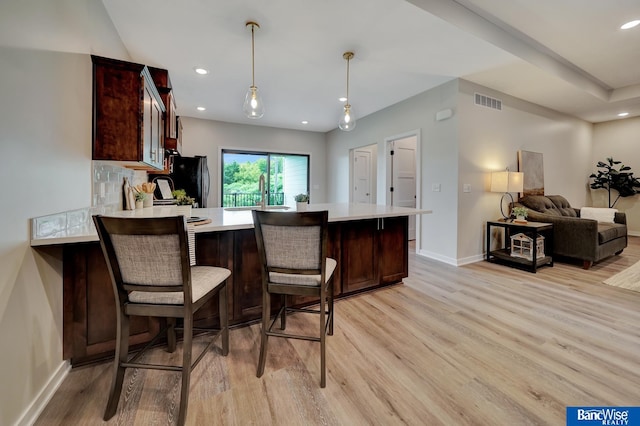 kitchen featuring a kitchen bar, light hardwood / wood-style flooring, kitchen peninsula, and tasteful backsplash