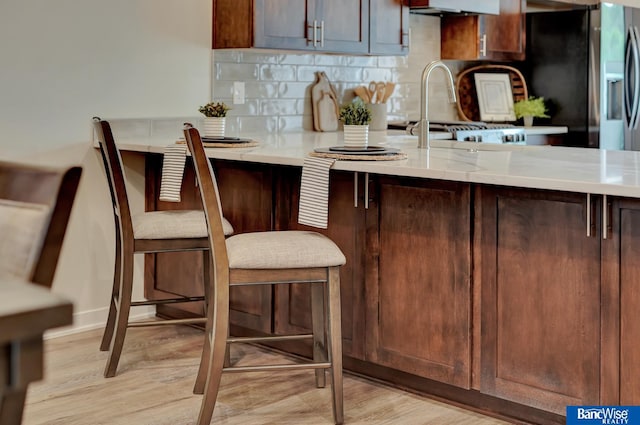 kitchen with a kitchen bar, light hardwood / wood-style floors, backsplash, and kitchen peninsula