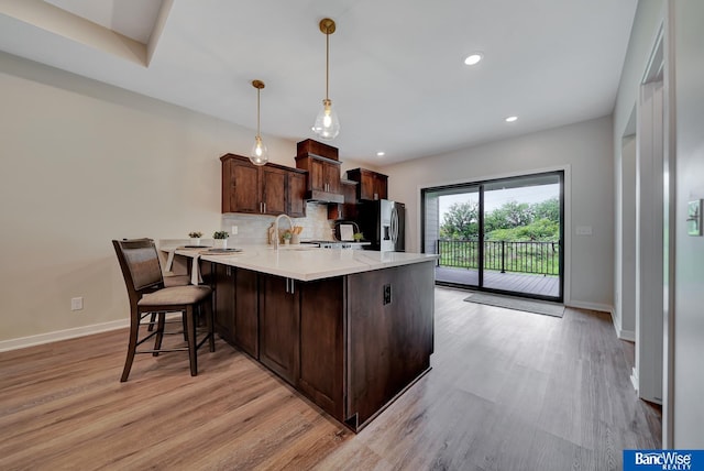 kitchen featuring dark brown cabinetry, tasteful backsplash, hanging light fixtures, light hardwood / wood-style flooring, and stainless steel refrigerator with ice dispenser