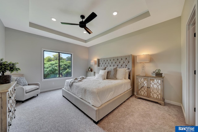 bedroom with light carpet, ceiling fan, and a raised ceiling