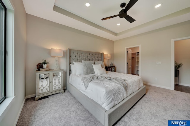 carpeted bedroom featuring a tray ceiling, ceiling fan, a walk in closet, and a closet